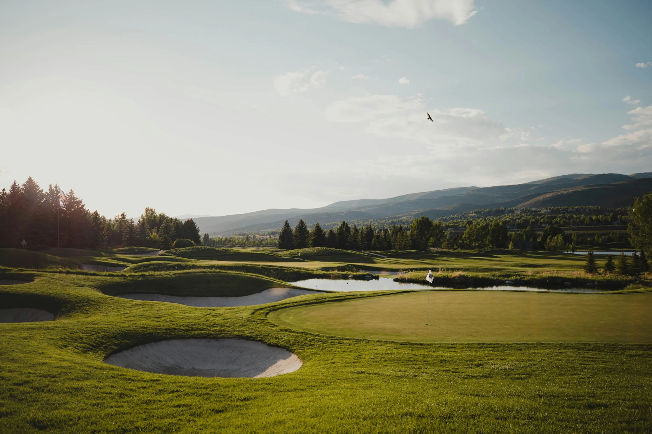 Sólin lýsir upp grænar golfbrautir, sandglompur og fjöll í fjarska